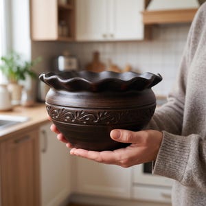May include: A dark brown ceramic bowl with a scalloped, wavy rim and a decorative embossed pattern featuring swirling leaf-like motifs around the upper section. The bowl has a smooth, rounded base and a deep, wide opening for serving food.