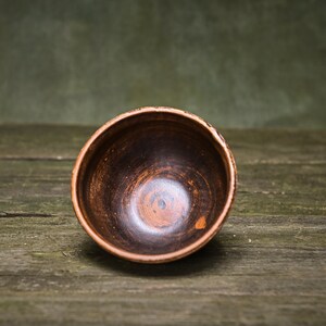 May include: A brown ceramic bowl with a dark brown interior. The bowl is sitting on a wooden surface.