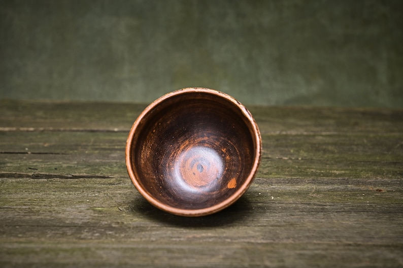 May include: A brown ceramic bowl with a dark brown interior. The bowl is sitting on a wooden surface.