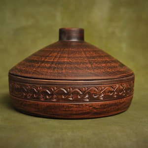 May include: A brown ceramic covered dish with a decorative floral design around the rim.