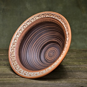 May include: A brown ceramic bowl with a white floral design around the rim. The bowl has a spiral pattern on the inside.