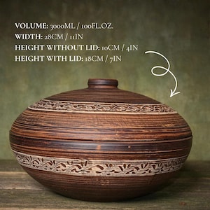 May include: A brown ceramic lidded bowl with horizontal grooves and a carved leaf pattern. Text: VOLUME: 3000ML / 100FL.OZ. WIDTH: 28CM / 11IN HEIGHT WITHOUT LID: 10CM / 4IN HEIGHT WITH LID: 18CM / 7IN. The bowl has a rounded shape and a matching lid.