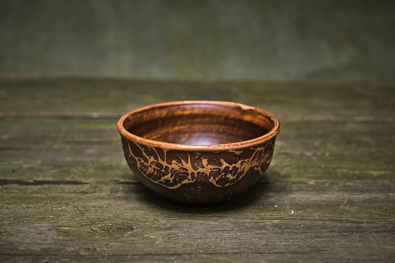 May include: A brown ceramic bowl with a decorative pattern on a wooden surface.