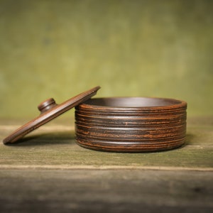 May include: A brown ceramic container with a lid. The container has a textured, striped design. The lid is slightly ajar.