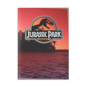 Puede incluir: Cuaderno con el logotipo de Jurassic Park, silueta de dinosaurio y escena de atardecer. La cubierta brillante presenta una paleta de colores de rojo, naranja y morado. Ideal para tomar notas y hacer bocetos.