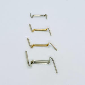 May include: Four metal clasps, two gold and two silver, with a curved design. The clasps are arranged vertically in order of size, with the smallest at the top and the largest at the bottom.