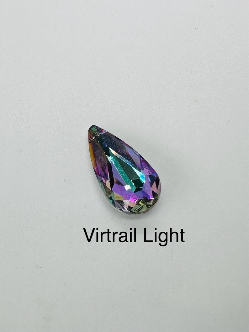 Op de afbeelding: Een druppelvormig kristal met een facetontwerp, dat een spectrum aan kleuren weergeeft, waaronder paars, groen en goud. De tekst "Virtrail Light" is eronder gedrukt. Het kristal staat tegen een witte achtergrond.