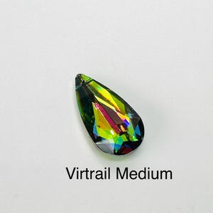 Op de afbeelding: Een druppelvormig kristal met een levendige, iriserende afwerking. Het kristal toont een spectrum aan kleuren, waaronder groen, geel en blauw, met de tekst "Virtrail Medium" eronder. Het kristal staat tegen een witte achtergrond.