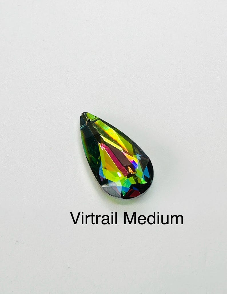 Op de afbeelding: Een druppelvormig kristal met een levendige, iriserende afwerking. Het kristal toont een spectrum aan kleuren, waaronder groen, geel en blauw, met de tekst "Virtrail Medium" eronder. Het kristal staat tegen een witte achtergrond.