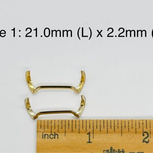 May include: Two gold-colored metal watch band spring bars, measuring 21.0mm in length and 2.2mm in width. The spring bars are shown next to a ruler for size reference.
