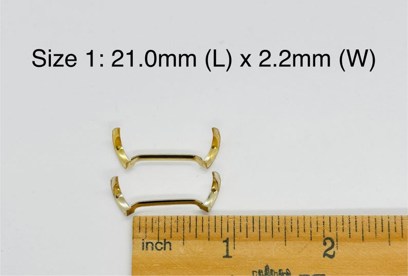 May include: Two gold-colored metal watch band spring bars, measuring 21.0mm in length and 2.2mm in width. The spring bars are shown next to a ruler for size reference.
