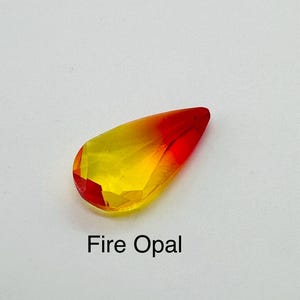 Op de afbeelding: Een gefacetteerde, druppelvormige vuuropaal edelsteen. De edelsteen gaat over van een levendig rood aan de punt naar een heldergele basis. De tekst "Fire Opal" is eronder in het zwart gedrukt.