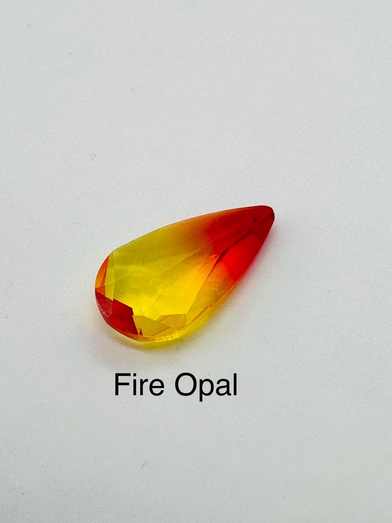 Op de afbeelding: Een gefacetteerde, druppelvormige vuuropaal edelsteen. De edelsteen gaat over van een levendig rood aan de punt naar een heldergele basis. De tekst "Fire Opal" is eronder in het zwart gedrukt.