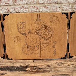 May include: A three-panel wooden screen featuring a laser-etched design of gears and cogs. The screen is made from light brown wood with black metal accents.