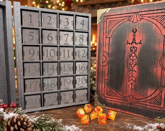 May include: A wooden advent calendar with twenty-four numbered drawers in a grey finish, paired with a matching red and black hinged box featuring a sword graphic composed of polyhedral dice shapes. Several orange and yellow dice sit in front.