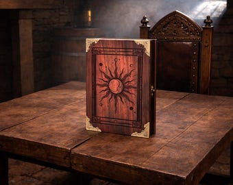 May include: A wooden book with a sun and moon design on the cover, with gold-coloured corner protectors. The book is open on a wooden table, with a dark wooden chair in the background.