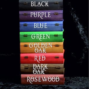 May include: A vertical stack of eight rectangular wooden boxes, each featuring metal hinges and white text labels: Black, Purple, Blue, Green, Golden Oak, Red, Dark Oak, and Rosewood. The boxes are finished in distinct wood stains.