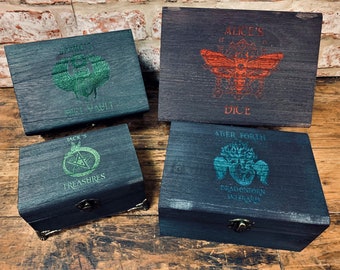 May include: Four wooden boxes with different designs. Each box has a different name and image. The first box says "Jack's Treasures" and has a pentagram. The second box says "Alice's Dice" and has a moth. The third box says "Aber Forth Dragonborn Wizard" and has a dragon. The fourth box says "Ermius First Vault" and has a scarab.