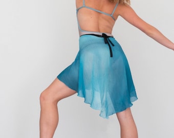 May include: A woman wearing a light blue leotard with a black ribbon and a turquoise sheer skirt. She is wearing ballet shoes and is posing with one leg raised.