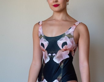 May include: A black swimsuit with a floral print featuring pink and green irises. The swimsuit has a scoop neck and a racerback style.