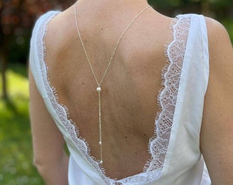 May include: A white, sleeveless top with a lace trim around the back neckline. A delicate silver chain with pearls hangs down the back.