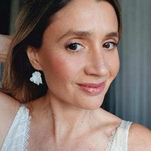 Peut inclure: Une femme portant un haut en dentelle blanche avec une paire de boucles d'oreilles en forme de fleur blanche.