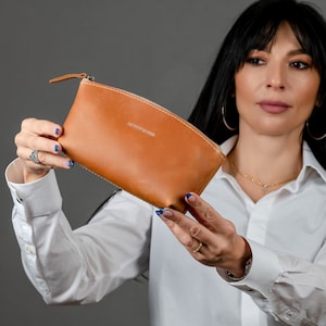 May include: A brown leather zippered pouch with the text "The Leather Studio" embossed on the front.