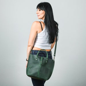 May include: A dark green leather tote bag with a top handle and a long shoulder strap. The bag has a front pocket and a zipper closure.