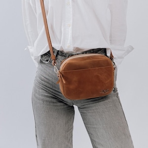 May include: A brown leather crossbody bag with a flap closure and a silver buckle. The bag has a small, rectangular shape and a strap that can be adjusted to fit comfortably across the body.