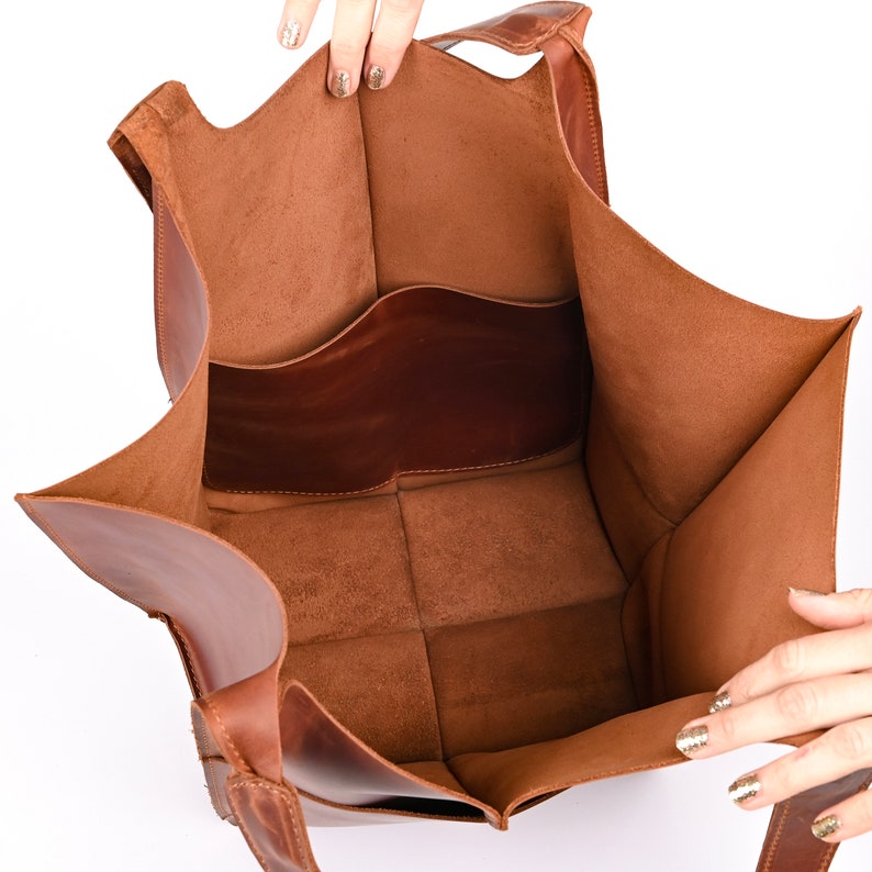 Puede incluir: Vista abierta de un bolso tote de cuero marr&oacute;n con un interior estructurado. El bolso tiene forma rectangular con un compartimento principal grande y un bolsillo m&aacute;s peque&ntilde;o. El cuero tiene un grano natural y un tono c&aacute;lido y terroso.