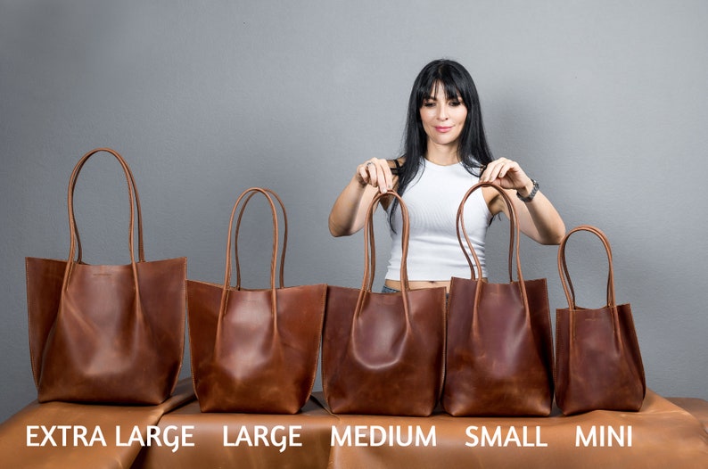 May include: Five brown leather tote bags of different sizes lined up on a table. The bags are labeled "Extra Large", "Large", "Medium", "Small", and "Mini".