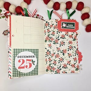May include: Open journal with Christmas-themed pages. One page has a grid pattern, the other has a floral design. A tag reads "Merry Christmas" with a Santa illustration. The date "December 25" is displayed on a round sticker.