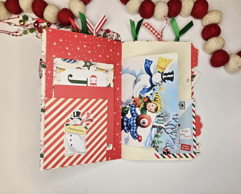 May include: Open Christmas-themed journal with red and white striped and star-patterned pages. Features a snowman illustration and a vintage winter scene. Includes pockets and decorative ribbons. A festive holiday craft.