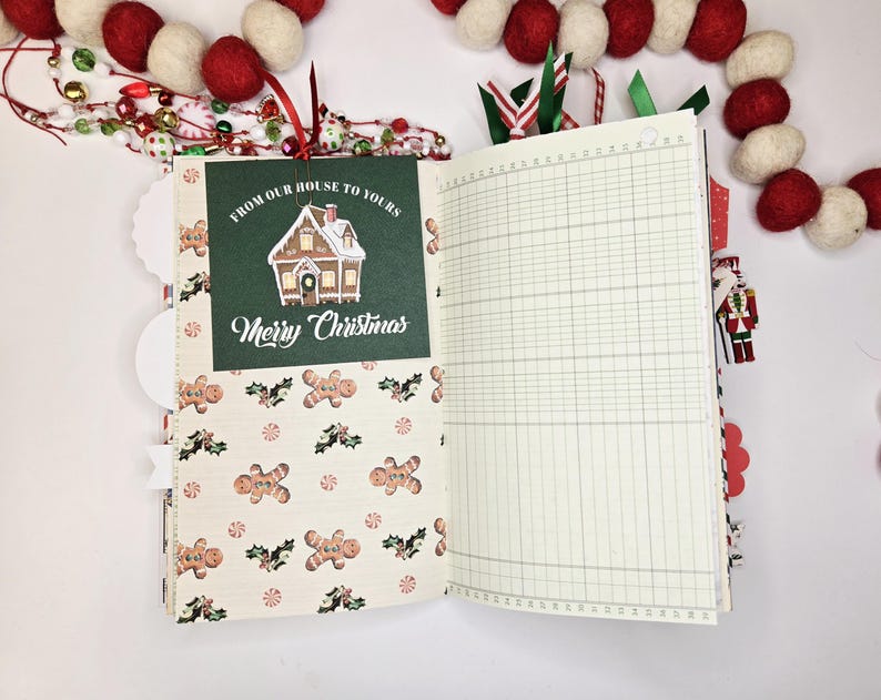 May include: Open journal with Christmas-themed pages. One page features a green card with a house illustration and the text "From Our House to Yours" and "Merry Christmas." The other page is lined. Festive decorations surround the journal.