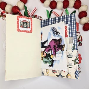 May include: Open journal with a vintage Christmas theme. The pages are cream-colored, with a decorative tag featuring a store. A winter scene illustration is visible. Festive decorations include a red and white garland.