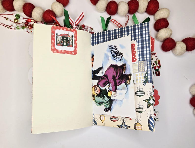 May include: Open journal with a vintage Christmas theme. The pages are cream-colored, with a decorative tag featuring a store. A winter scene illustration is visible. Festive decorations include a red and white garland.