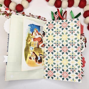 May include: Open Christmas-themed journal with a Santa Claus illustration and patterned pages. The journal features a festive design with red, green, and white accents, including a decorative garland.