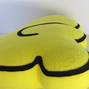 Op de afbeelding: Een geel pluche kussen in de vorm van een wolk met een zwarte omtrek.