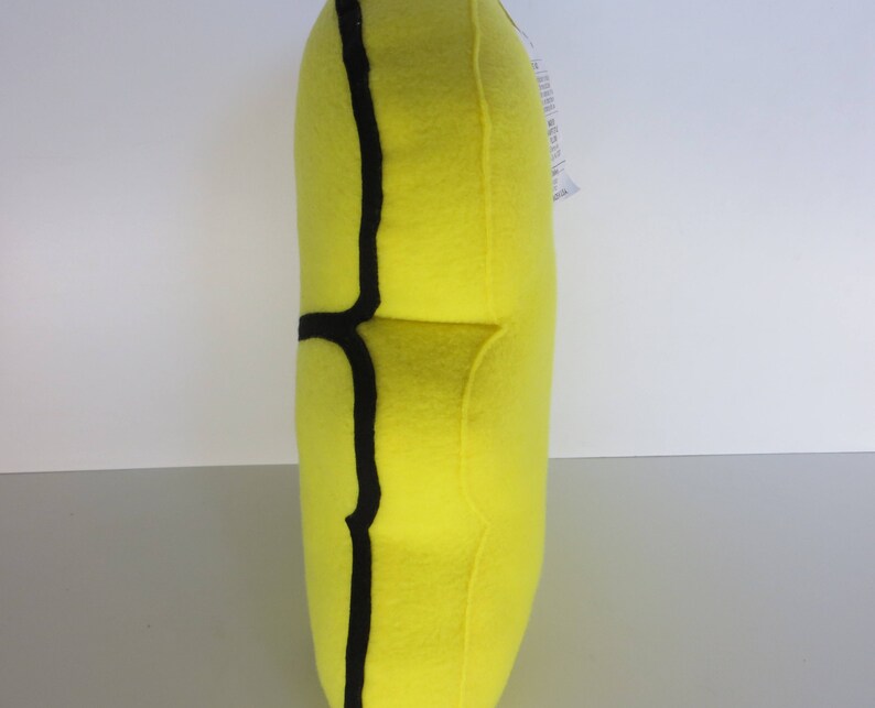 Op de afbeelding: Een geel pluche kussen met een zwarte omtrek in de vorm van een banaan.