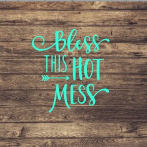May include: A teal blue sign with the text "Bless this hot mess" on a wood background.