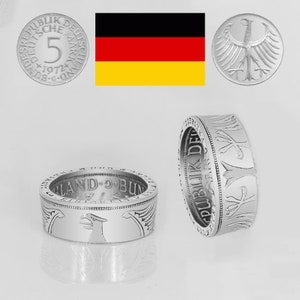 Könnte beinhalten: Zwei silberne Ringe aus deutschen 5-Deutsche-Mark-Münzen. Die Ringe tragen den Text "PUBLIK DEUTSCH LAND-BUND" und ein Adlerdesign.