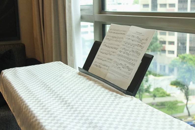 May include: A black music stand with sheet music on a white and gray checkered table top. The music stand is in front of a window with a view of a city.