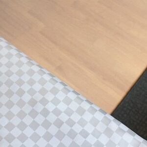 May include: A close-up of a white and gray checkered fabric with a light brown wooden surface and a dark gray textured surface in the background.