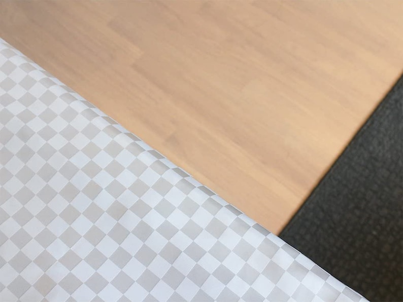 May include: A close-up of a white and gray checkered fabric with a light brown wooden surface and a dark gray textured surface in the background.