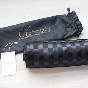 May include: A black fabric bag with a gold logo that says "Clairevoire". The bag is folded and sitting on a wooden surface. A white tag with the same logo is next to the bag.