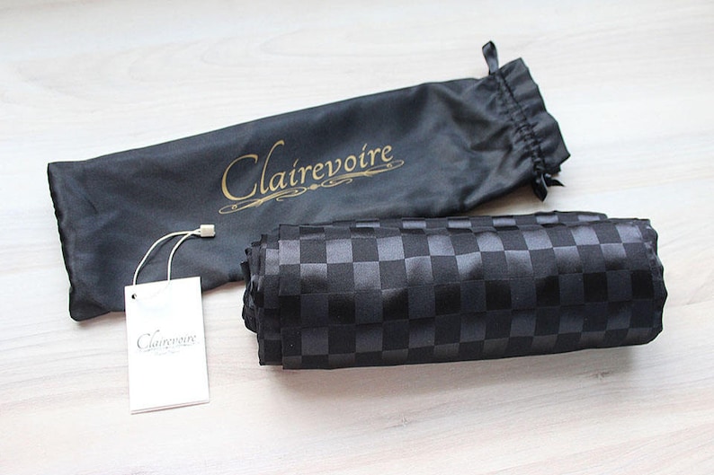 May include: A black fabric bag with a gold logo that says "Clairevoire". The bag is folded and sitting on a wooden surface. A white tag with the same logo is next to the bag.