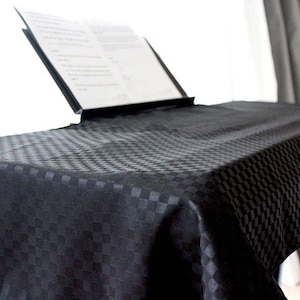 May include: Black checkered tablecloth with a music stand on top. The tablecloth is made of a soft, textured fabric.