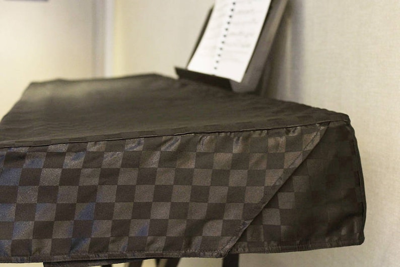 May include: Black checkered keyboard cover with a black music stand in the background.