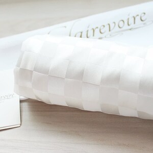 May include: White fabric with a checkered pattern, rolled up and placed on a white surface. The fabric is labeled "Clairevoire".