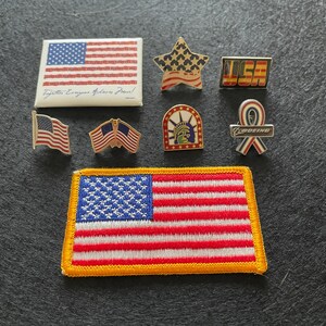 May include: A collection of patriotic pins and patches including a rectangular flag pin with text, a star-shaped flag pin, a USA block letter pin, a small waving flag pin, a crossed flag pin, a Statue of Liberty pin, a Boeing ribbon pin, and a flag patch.